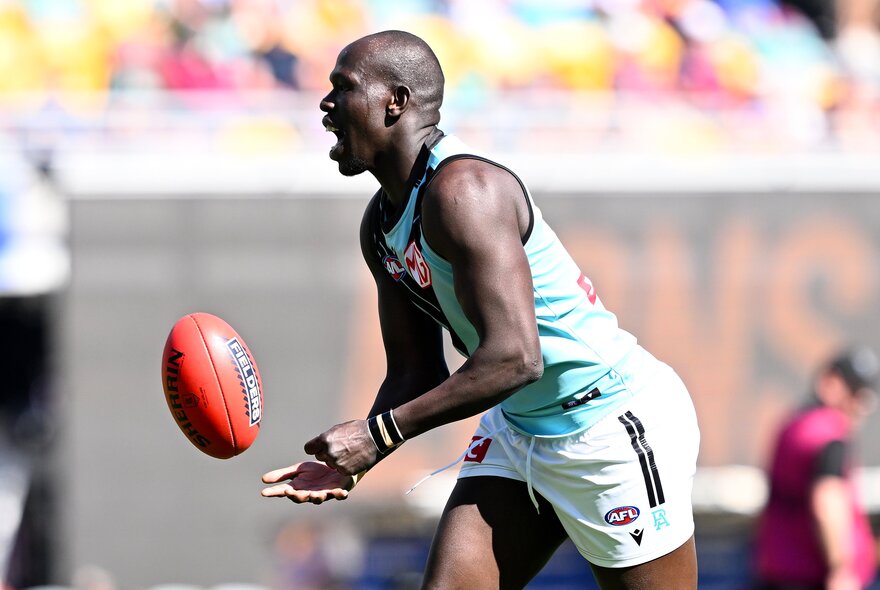 A Port Adelaide Power AFL player handballing a red football during a game.