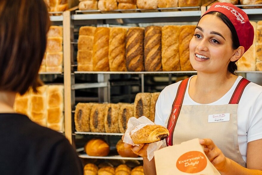 Bakers Delight staff member putting a pastry into a paper bag with a customer.