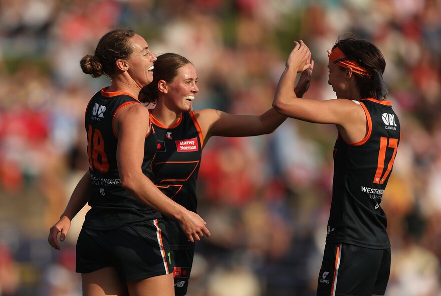 Three GWS Giants AFLW players celebrating on the field, coming together for a group huddle and a high five.