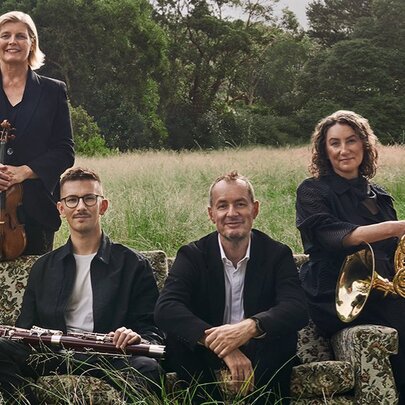 Four members of the Australian Chamber Orchestra, some holding their instruments, in a pastoral setting.