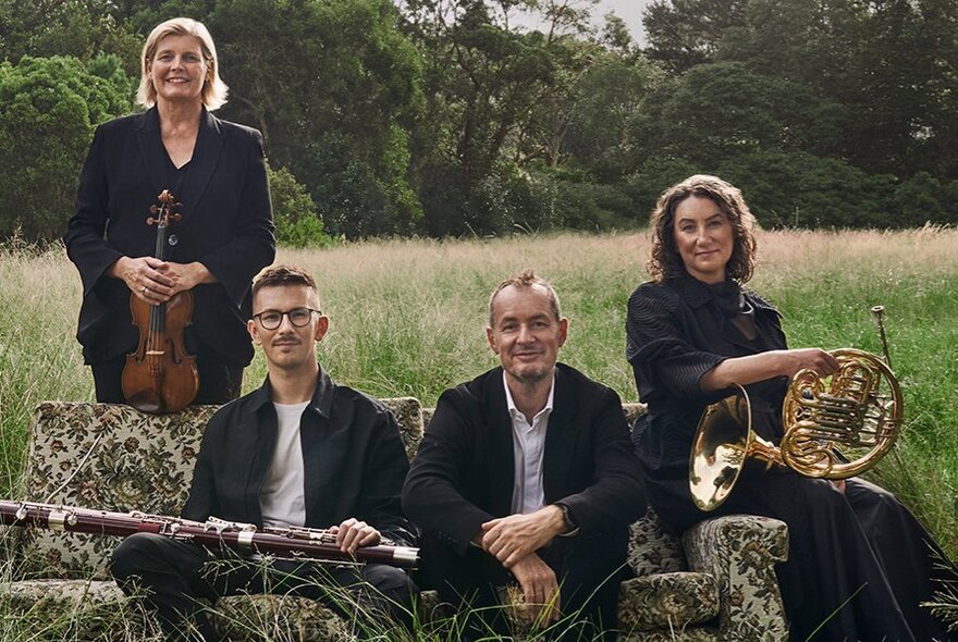 Four members of the Australian Chamber Orchestra, some holding their instruments, in a pastoral setting.