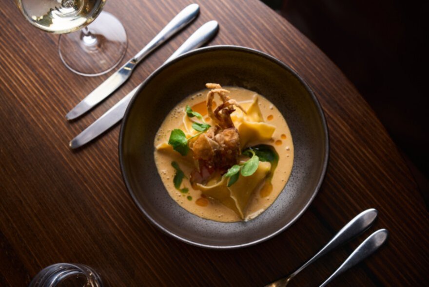 Top down view of a shallow brown bowl with food served in a creamy orange sauce, cutlery alongside.