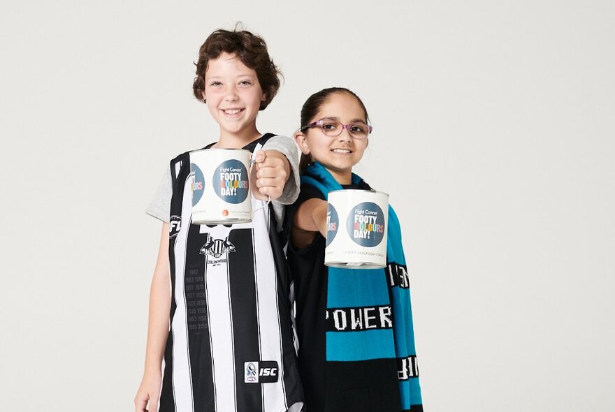 Two kids wearing footy colours, holding out mugs with the Fight For Cancer logo on them.