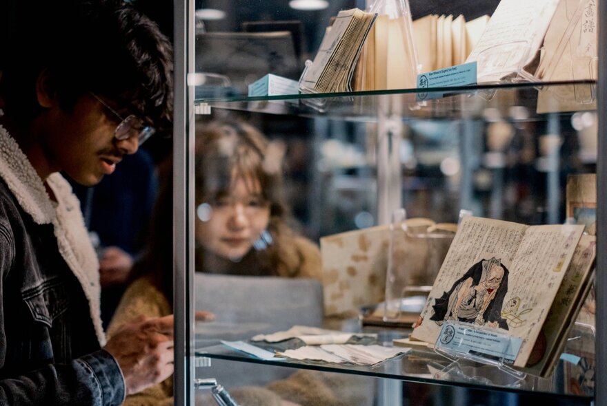 People looking at illustrated books on display in a glass cabinet.
