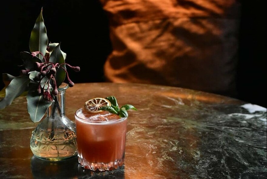 A cocktail on a table next to a dried flower arrangement