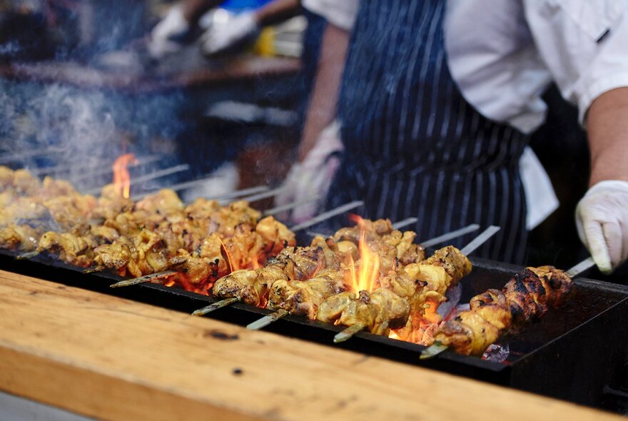 A chef grilling skewers of meat over open flames.