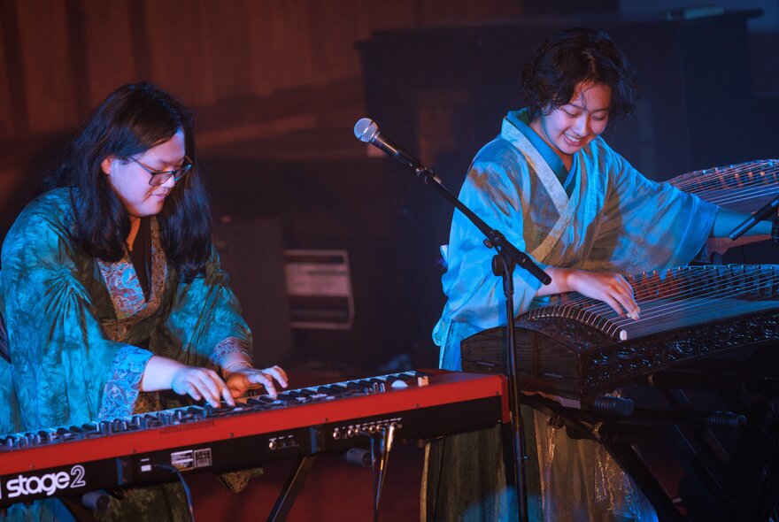 Two traditional Chinese performers, one playing the Chinese guzheng and the other a modern keyboard.