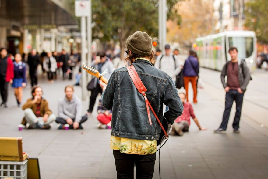 The back of a busker performing in a street in front of a handful of people. 