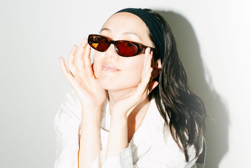 DJ Logic1000, a woman wearing sunglasses and smiling, her long hair held in place by a headband.