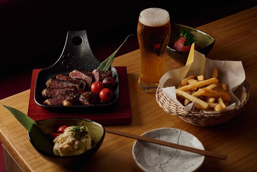 Japanese snack dishes on a table with a glass of beer, including chips and chopsticks.