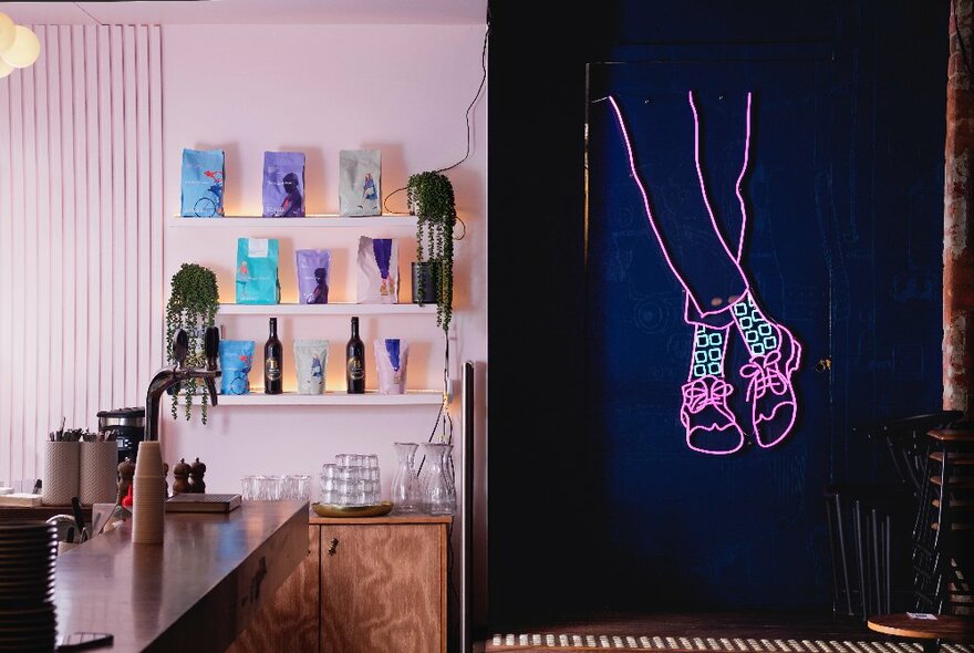 Cafe interior with pink walls, backlit shelves and pink artwork of crossed legs with shoes.