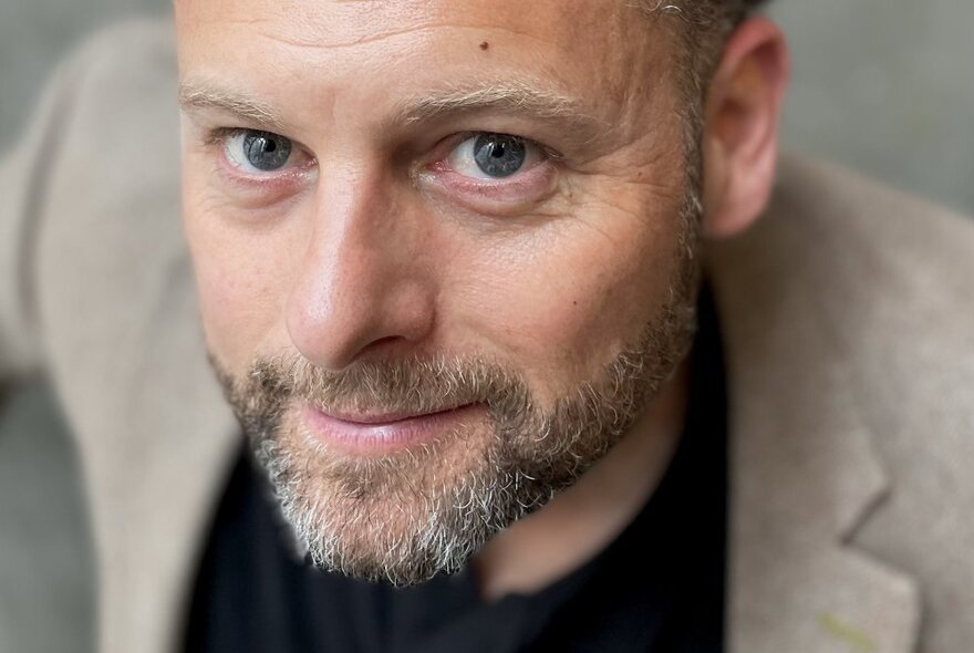 Man with greying beard looking up, wearing a pale linen jacket.