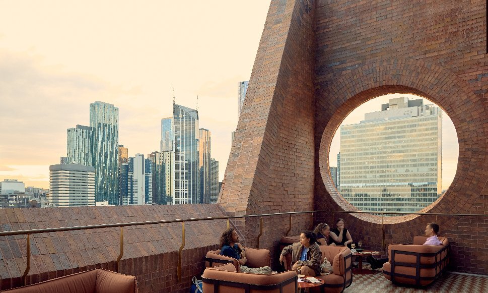 Two groups of friends are on a rooftop bar with a large circular window.