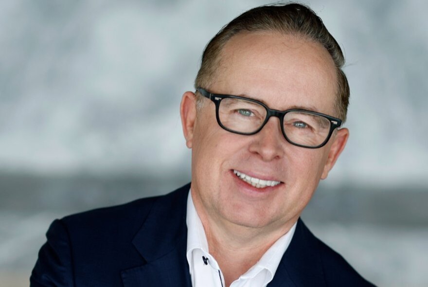 Head-shot of Alan Joyce, a prominent middle-aged businessman, he wears glasses, a white shirt and a dark suit jacket.