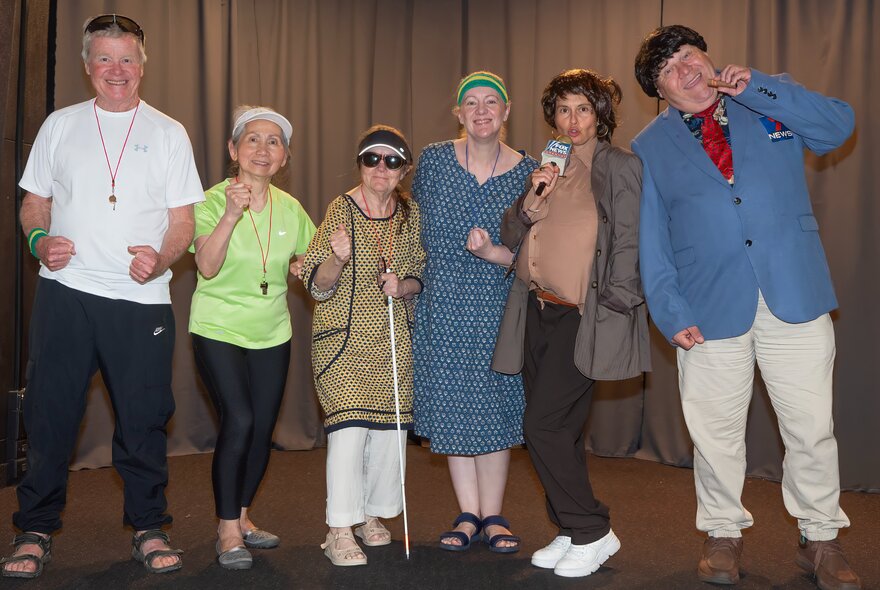 A local community theatre cast or group posing on stage in front of a curtain, some dressed in costumes. 