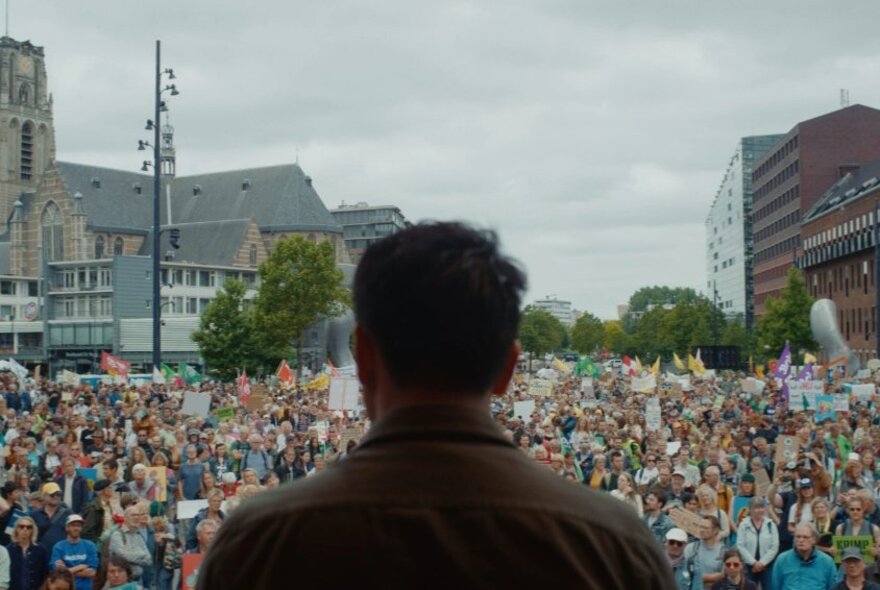 The back of a man standing in front of a massive crowd of people in a city. 