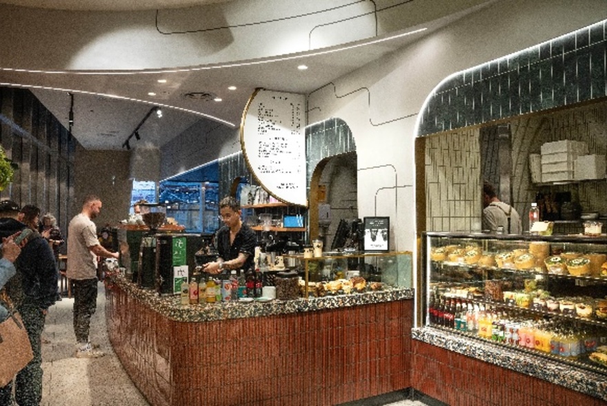 Interior of Axil Coffee at Collins Arch, with people standing inside waiting to order coffee and food at the large service counter.