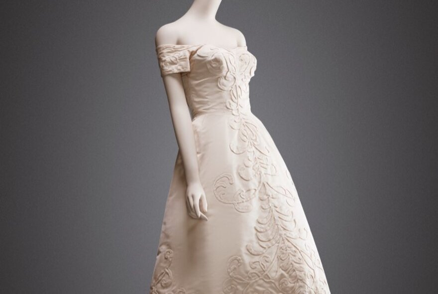 A strapless white gown with heavy embroidery, displayed on a mannequin.