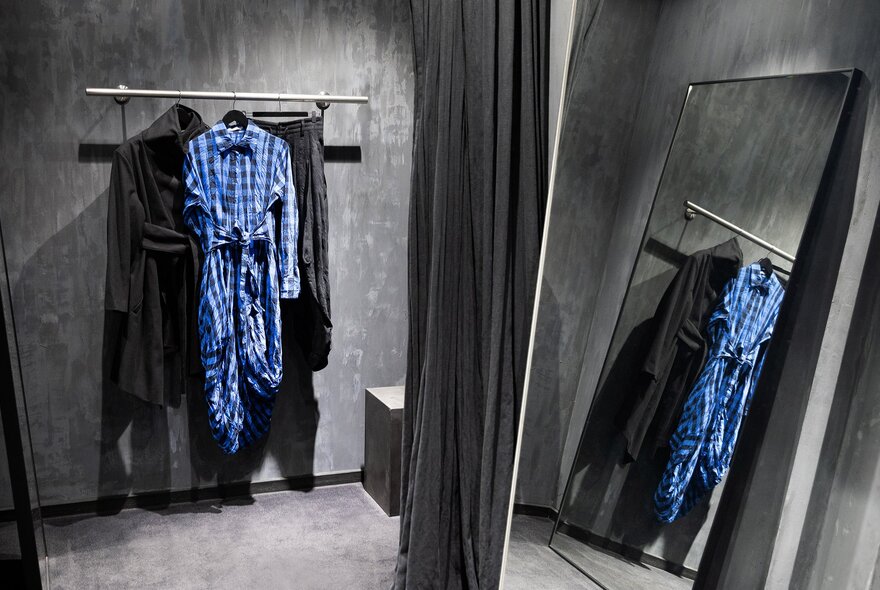 A change room inside the store Et Al, with three garnets hanging on a rack, a long black curtain pulled to one side.