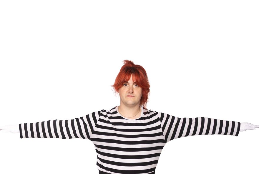 Woman with red hair wearing a striped top, her arms outstretched.