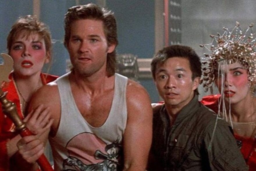 A still from a film showing one man in a singlet, a Chinese man and two elaborately-costumed women looking at something with surprise and horror.