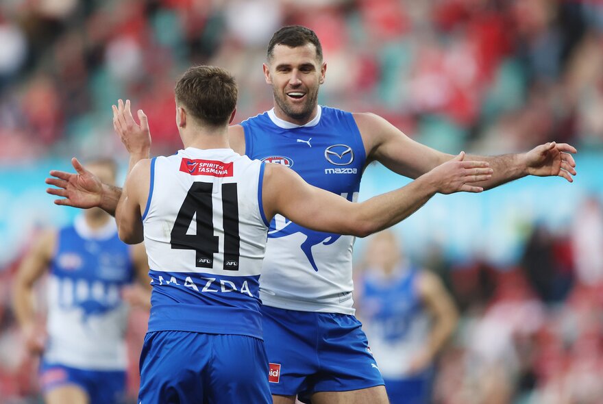 North Melbourne AFL football players clapping hands during a match.