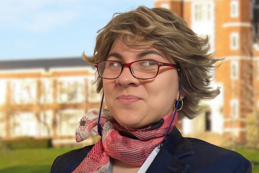 A woman dressed in the guise of a school principal, with spectacles, pursed lips and a silk scarf around her neck.