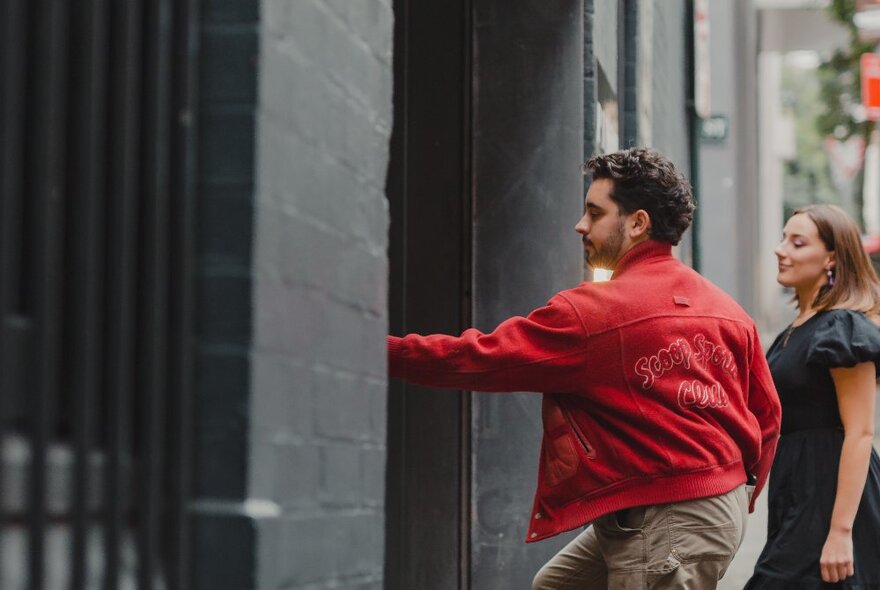 Two people on a street, pushing a door opening and walking inside.