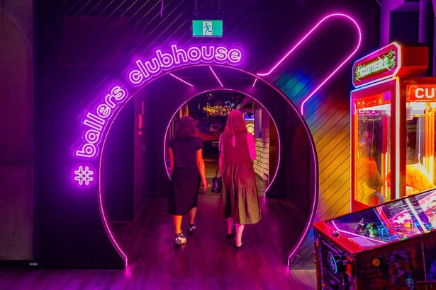 Two friends walking through a neon lit doorway shaped like a table tennis paddle.