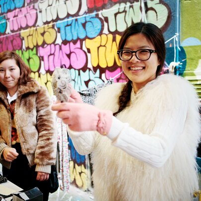 Two women at a secondhand staff with posters and graffiti on the wall behind them.