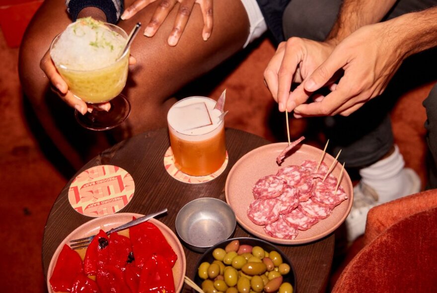 People seated around plates of bar snacks holding drinks.