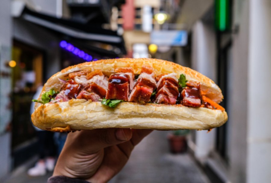 A banh mi held in front of a laneway.