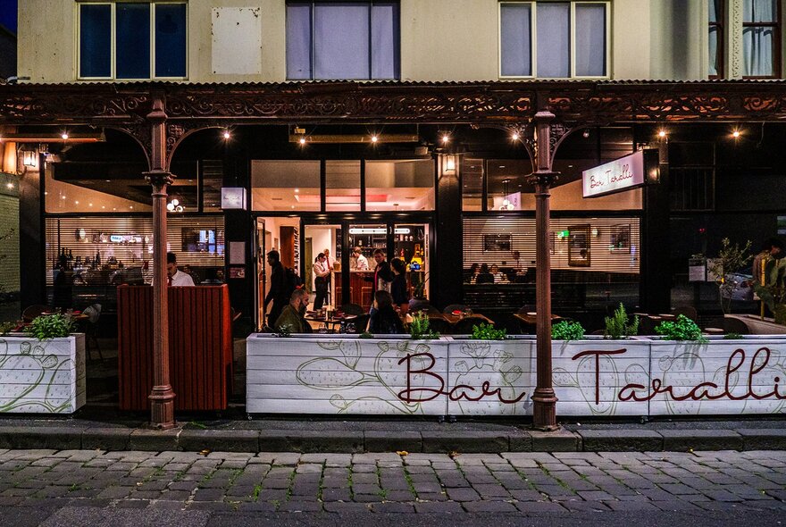 The exterior of a restaurant with festoon lights and outdoor seating.