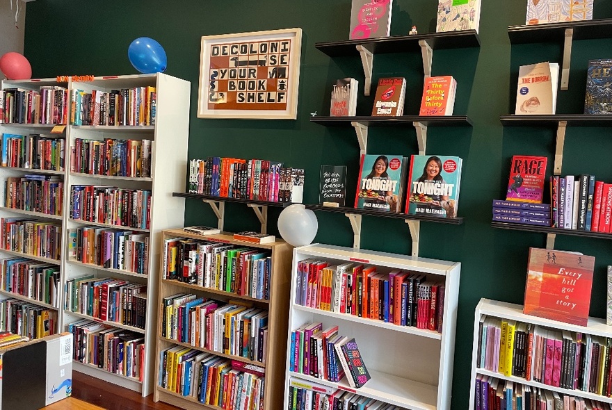 Bookstore interior with shelves of colourful books against dark green wall.