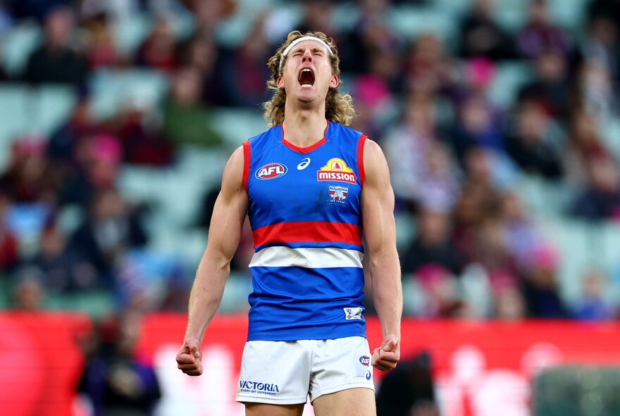 A Western Bulldogs AFL football player with an open mouth yelling and clenched fists during a match, cheering himself on.