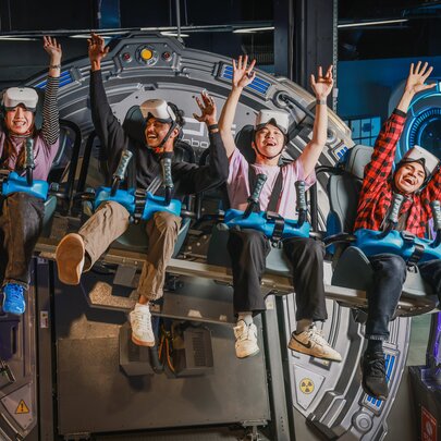 Four young people holding their arms up on a VR ride.