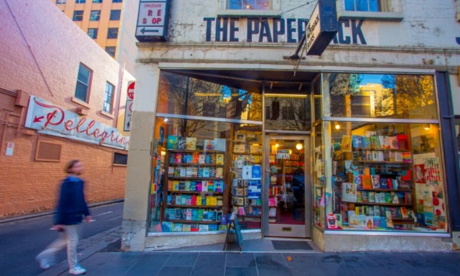 A person walking past an old book store with windows full of rows of books on display