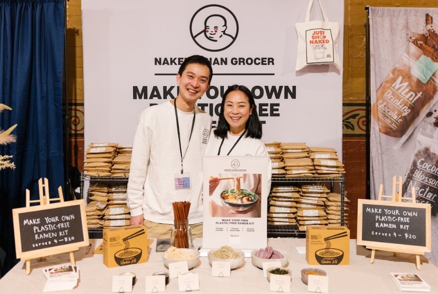 A smiling couple standing behind their stall selling food products at a food market.