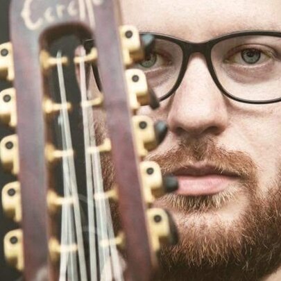 The musician Alessandro Santacaterina, a bearded man wearing glasses, posing with a musical instrument, a chitarra battente.