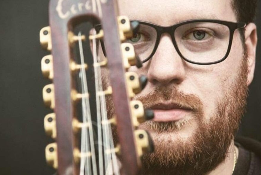 The musician Alessandro Santacaterina, a bearded man wearing glasses, posing with a musical instrument, a chitarra battente.