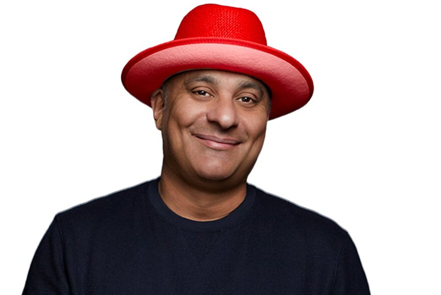 Comedian Russell Peters smiling and wearing a red hat. 