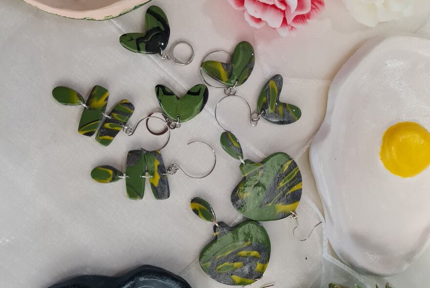 Pairs of green clay earrings displayed next to a tray designed like a fried egg.