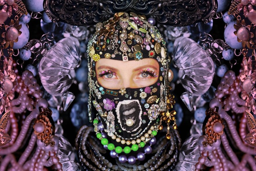 A woman's eyes - the only part of her face visible - looking out of an elaborately beaded and decorated face balaclava and costume. 