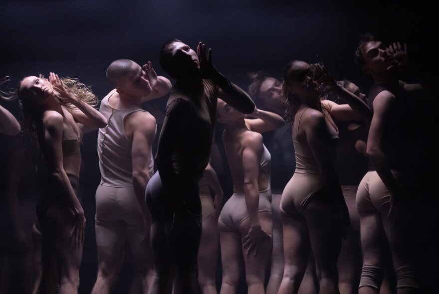 A large group of dancers moving in unison on a stage, all wearing skin-coloured tight-fitting dancewear.