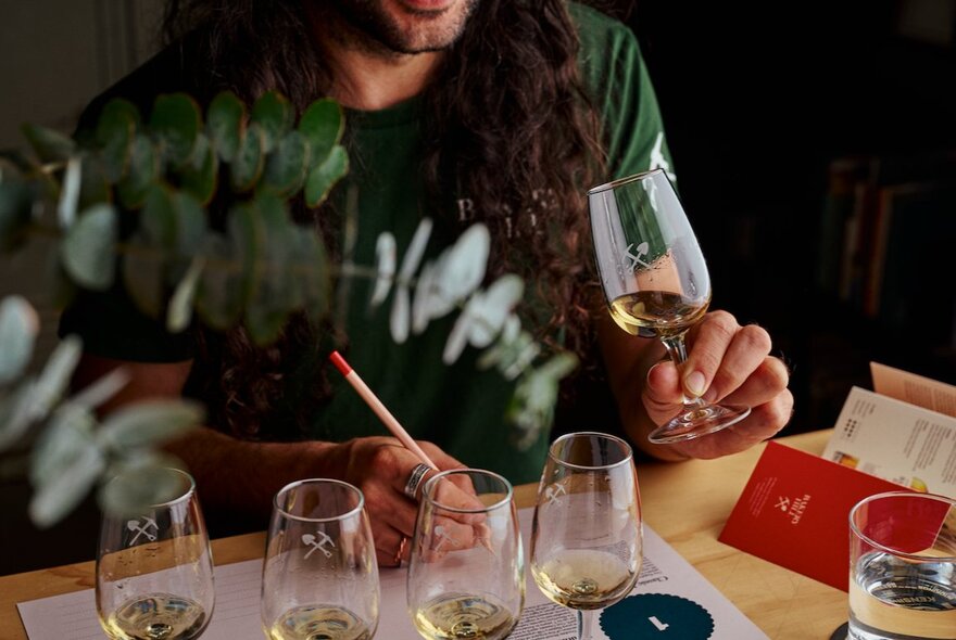 A person participating in a guided spirits tasting session, holding a tasting glass while taking notes next to a flight of small glasses.