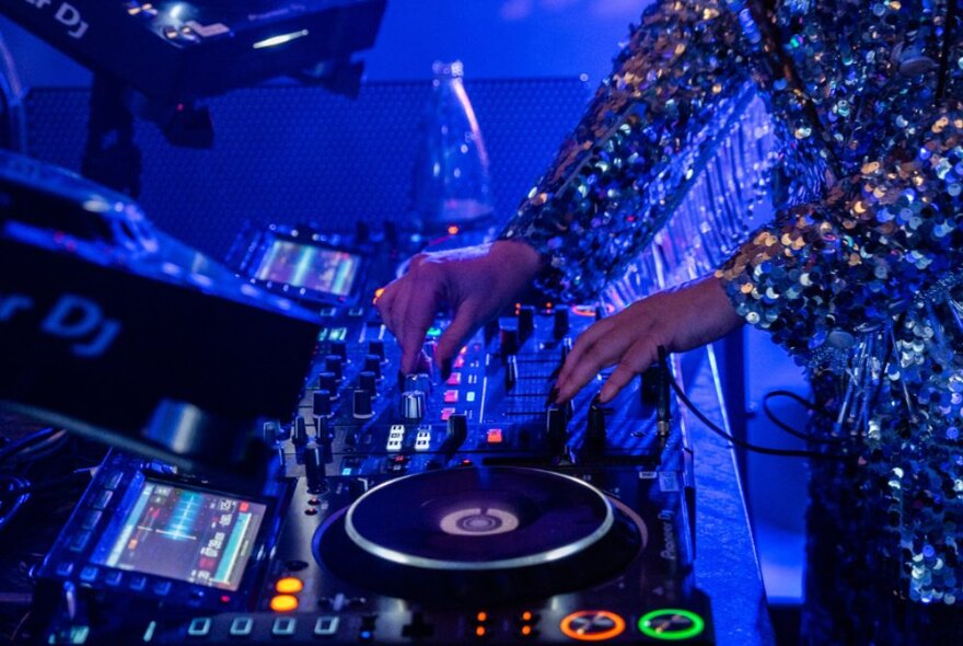 A DJ fiddling with the controls of a DJ desk at a bar.