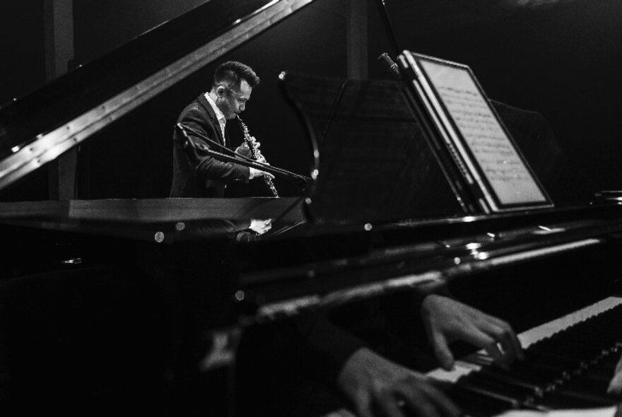 Pianist and oboe player performing under angled lighting in a dark space.