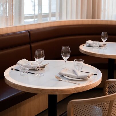 Dining area with a curved banquette, round tables and rattan chairs at Ho Jiak. 