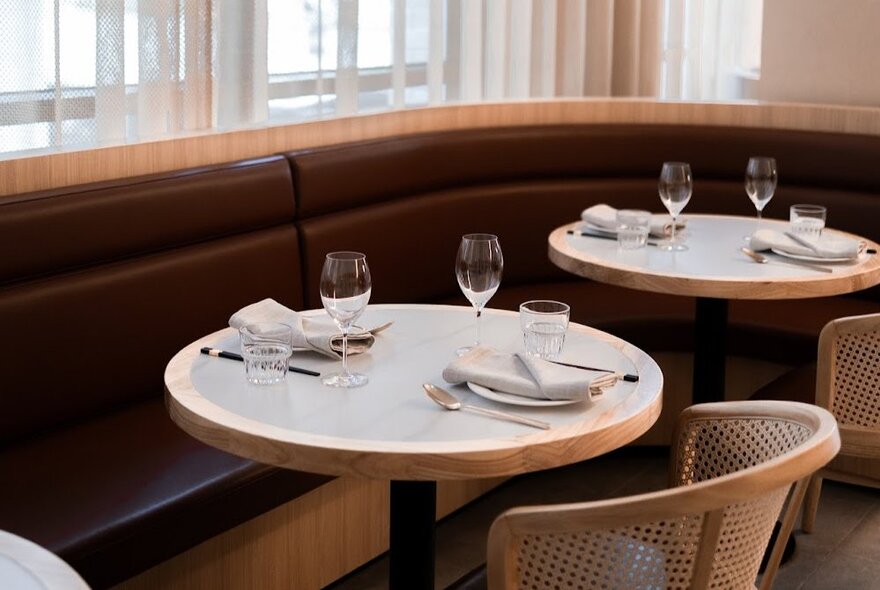 Dining area with a curved banquette, round tables and rattan chairs at Ho Jiak. 