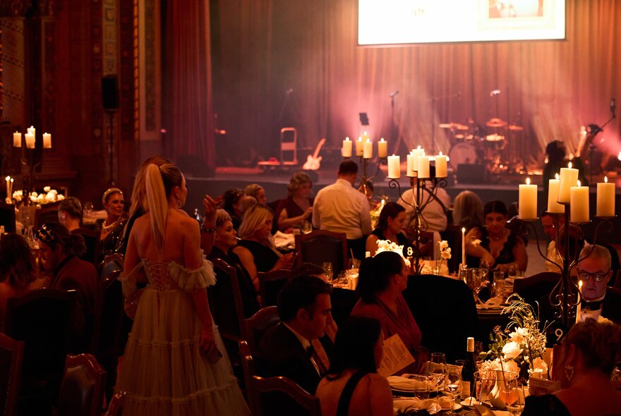 People dining at dimly lit tables with candles in a large formal venue.
